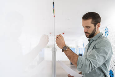 Businessman checking paper while writing on whiteboard at office - DIGF14873