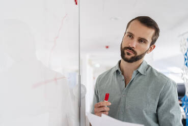Thoughtful professional looking at whiteboard while working in office - DIGF14875
