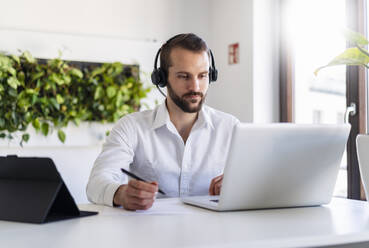 Entrepreneur with headphones working on laptop at office - DIGF14891