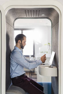 Männlicher Unternehmer bei einer Besprechung am Laptop in einer Telefonzelle im Büro - DIGF14900