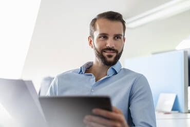 Geschäftsmann mit Papier und digitalen Tablet lächelnd im Büro - DIGF14903