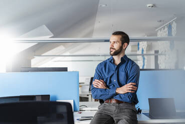 Unternehmer mit verschränkten Armen auf dem Schreibtisch sitzend im Büro - DIGF14920