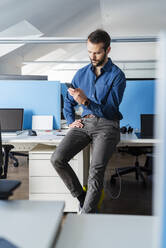 Young businessman using mobile phone while sitting on desk at office - DIGF14921