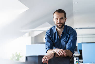 Smiling businessman leaning on chair at office - DIGF14924