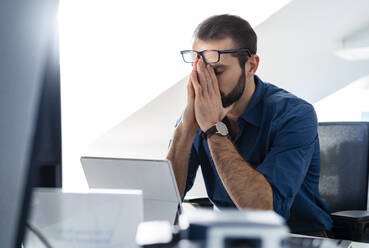 Businessman sitting with head in hands at office - DIGF14929