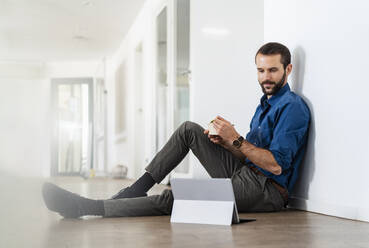 Young businessman looking at digital tablet while eating food at office - DIGF14935