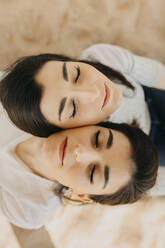 Young female twins with eyes closed on sand - ARTF00040