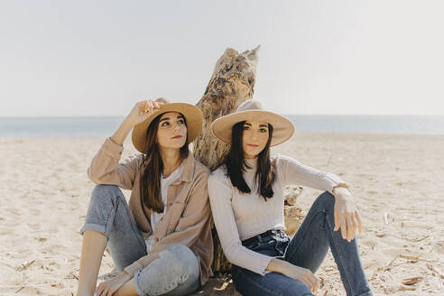 Weibliche Zwillinge sitzen Seite an Seite am Strand an einem sonnigen Tag - ARTF00042