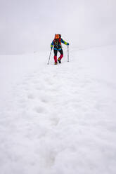 Männlicher Wanderer, der einen schneebedeckten Berg mit Wanderstöcken besteigt - MCVF00736