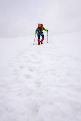 Male hiker climbing snowcapped mountain with hiking poles - MCVF00736