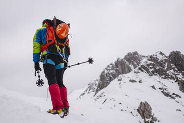 Älterer Mann, der einen Rucksack trägt, während er mit Steigeisen und Wanderstöcken auf einem schneebedeckten Berg wandert - MCVF00738