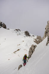 Älterer Wanderer steht an einem Felsen auf einem schneebedeckten Berg - MCVF00741