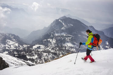 Männlicher Wanderer mit Rucksack und Wanderstock auf einem schneebedeckten Berg, der Steigeisen trägt - MCVF00743