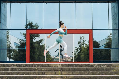 Aktive Sportlerin beim Laufen auf den Stufen an der Glaswand - MTBF00888