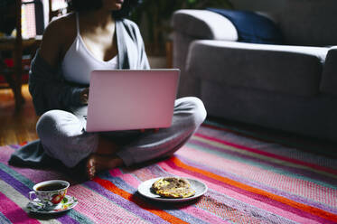 Frau, die einen Laptop benutzt, während sie auf dem Boden frühstückt - PGF00470