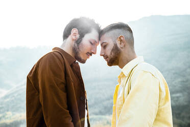 Homosexuelles Paar mit geschlossenen Augen steht von Angesicht zu Angesicht gegen den Himmel - DAF00001
