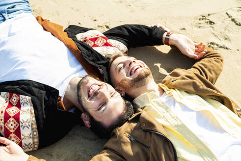 Fröhliches homosexuelles Paar hat Spaß, während es am Strand im Urlaub auf dem Sand liegt - DAF00002