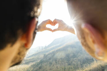 Gay couple doing heart shape with hands at beach - DAF00005