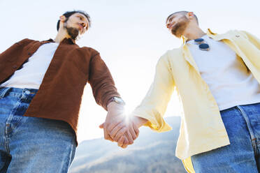 Homosexuelles Paar, das sich gegenseitig anschaut, während es die Hände gegen den Himmel hält - DAF00008