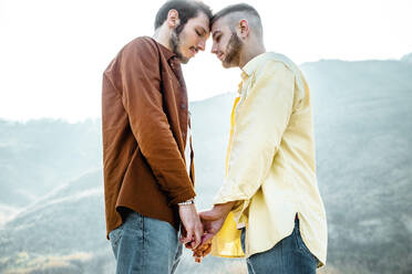 Homosexuelles Paar, das sich an den Händen hält und von Angesicht zu Angesicht gegen den Himmel steht - DAF00011