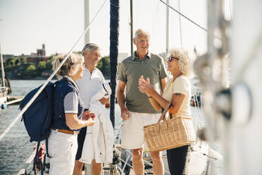 Male and female senior friends talking with each other while standing in boat on sunny day - MASF22281