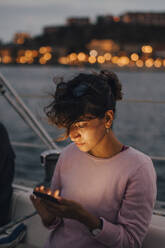 Mittlere erwachsene Frau, die ein Smartphone benutzt, während sie bei Sonnenuntergang in einem Boot sitzt - MASF22286