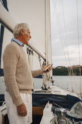Senior man navigating direction through smart phone while standing on boat during sunset - MASF22289