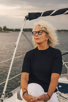 Ältere Frau mit geschlossenen Augen sitzt bei Sonnenuntergang auf einem Boot - MASF22295
