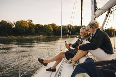Glückliches älteres Paar, das während des Sonnenuntergangs ein Mobiltelefon benutzt - MASF22297