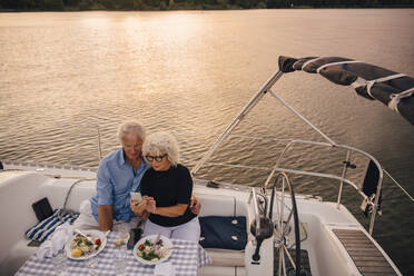 High angle view of senior couple taking selfie through mobile phone in sailboat during sunset - MASF22299