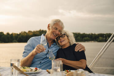 Glücklicher älterer Mann mit Arm um Frau mit Wein gegen das Meer in Boot - MASF22302