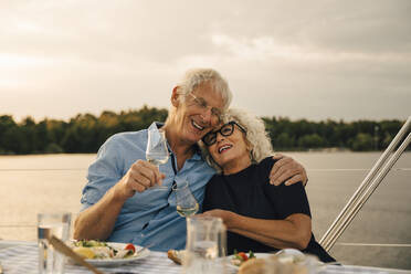 Happy senior man with arm around woman having wine against sea in boat - MASF22302