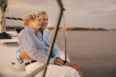Happy senior couple sitting on edge of sailboat during sunset - MASF22304