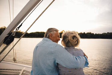 Senior man embracing woman while sitting in boat during sunset - MASF22305