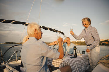 Cheerful senior couples toasting wineglasses in boat against sky on sunny day - MASF22306