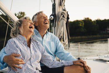 Fröhliches Paar, das lacht, während es seine Freizeit auf einem Segelboot verbringt - MASF22307