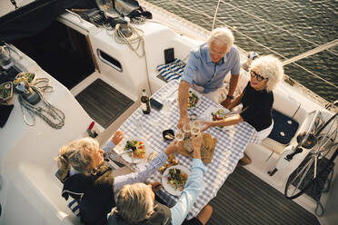 High angle view of male and female friends toasting wineglasses at table in boat - MASF22312