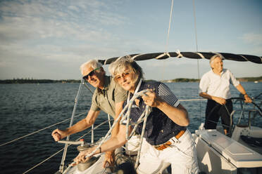 Älterer Mann dreht die Kurbel eines Bootes, während seine Freundin mit einem Seil vor dem Himmel steht - MASF22318