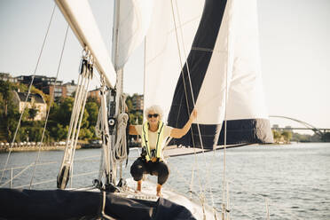 Ältere Frau hockt an einem Seil in einem Boot an einem sonnigen Tag - MASF22322