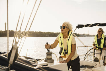 Ältere Frau segelt mit einer Freundin in einem Boot an einem sonnigen Tag - MASF22329