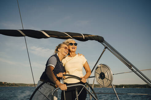 Fröhliche Freundinnen schauen weg, während sie in einem Boot vor dem Himmel stehen - MASF22331
