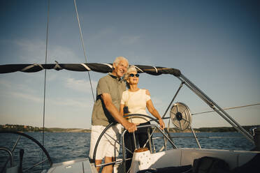 Smiling senior couple with arm around in sailboat against sky in sea - MASF22332