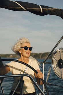Lächelnde ältere Frau beim Segeln im Meer an einem sonnigen Tag - MASF22334