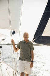 Porträt eines älteren Mannes, der ein Seil hält, während er in einem Boot auf dem Meer steht, an einem sonnigen Tag - MASF22336