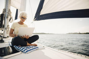 Ältere Frau arbeitet aus der Ferne beim Segeln auf einem Boot an einem sonnigen Tag - MASF22342