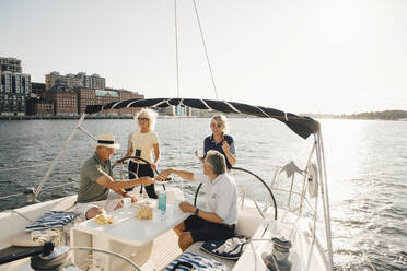 Senior couples having food while sitting in boat against clear sky - MASF22346