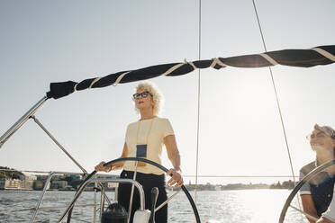 Senior woman sailing boat with female friend against clear sky on sunny day - MASF22347