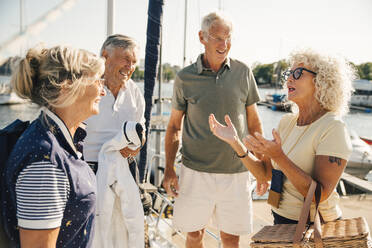 Smiling senior couples talking with each other on boat during sunny day - MASF22360