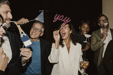 Cheerful business people enjoying with props during company party at night - MASF22369