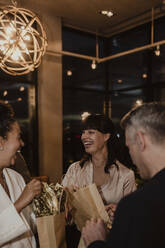 Männliche und weibliche Kollegen lachen, während sie Geschenktüten bei einer Firmenfeier halten - MASF22372